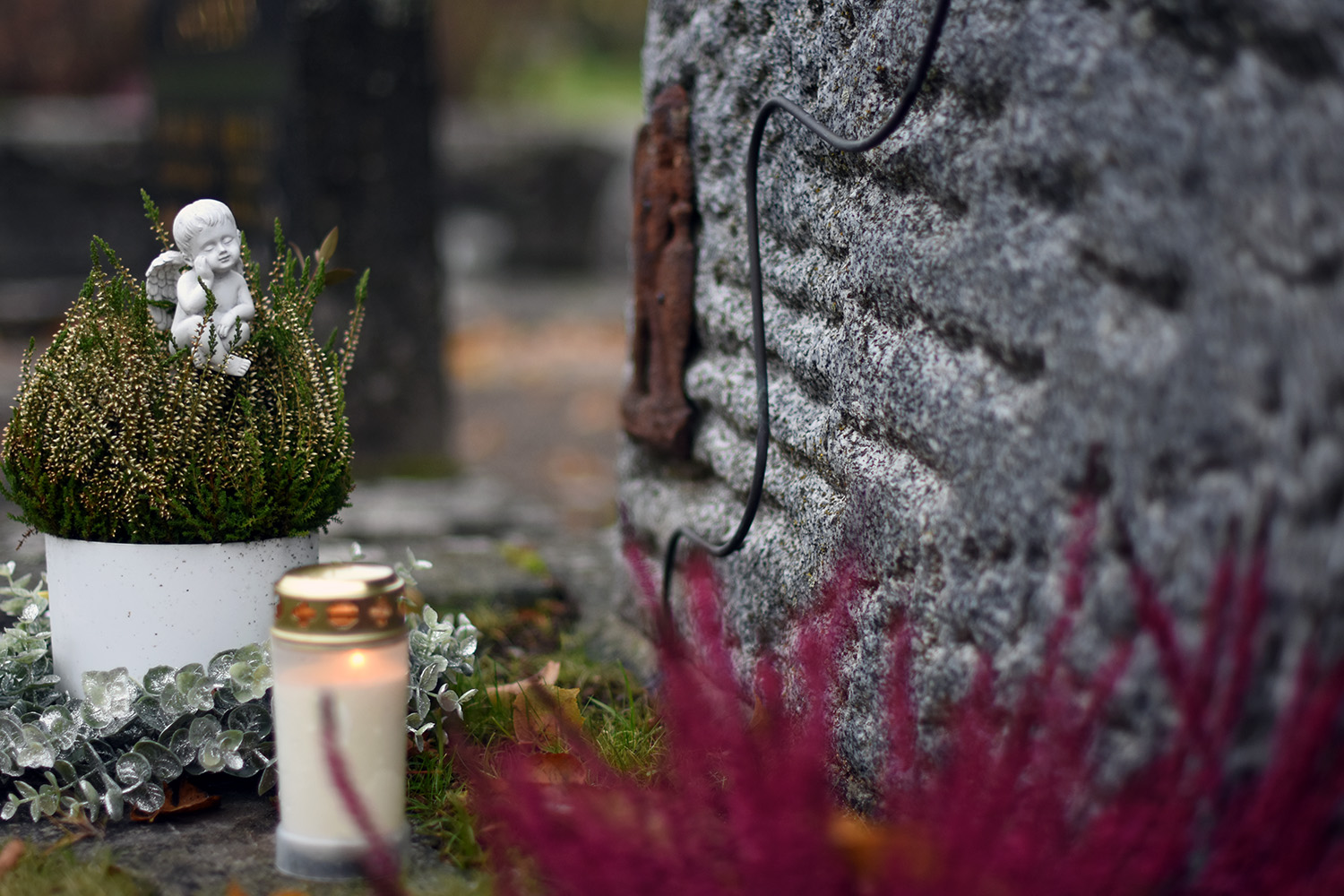 Hautakivi, jonka edessä valkoinen pieni enkelipatsas, kynttilä ja kukkia.