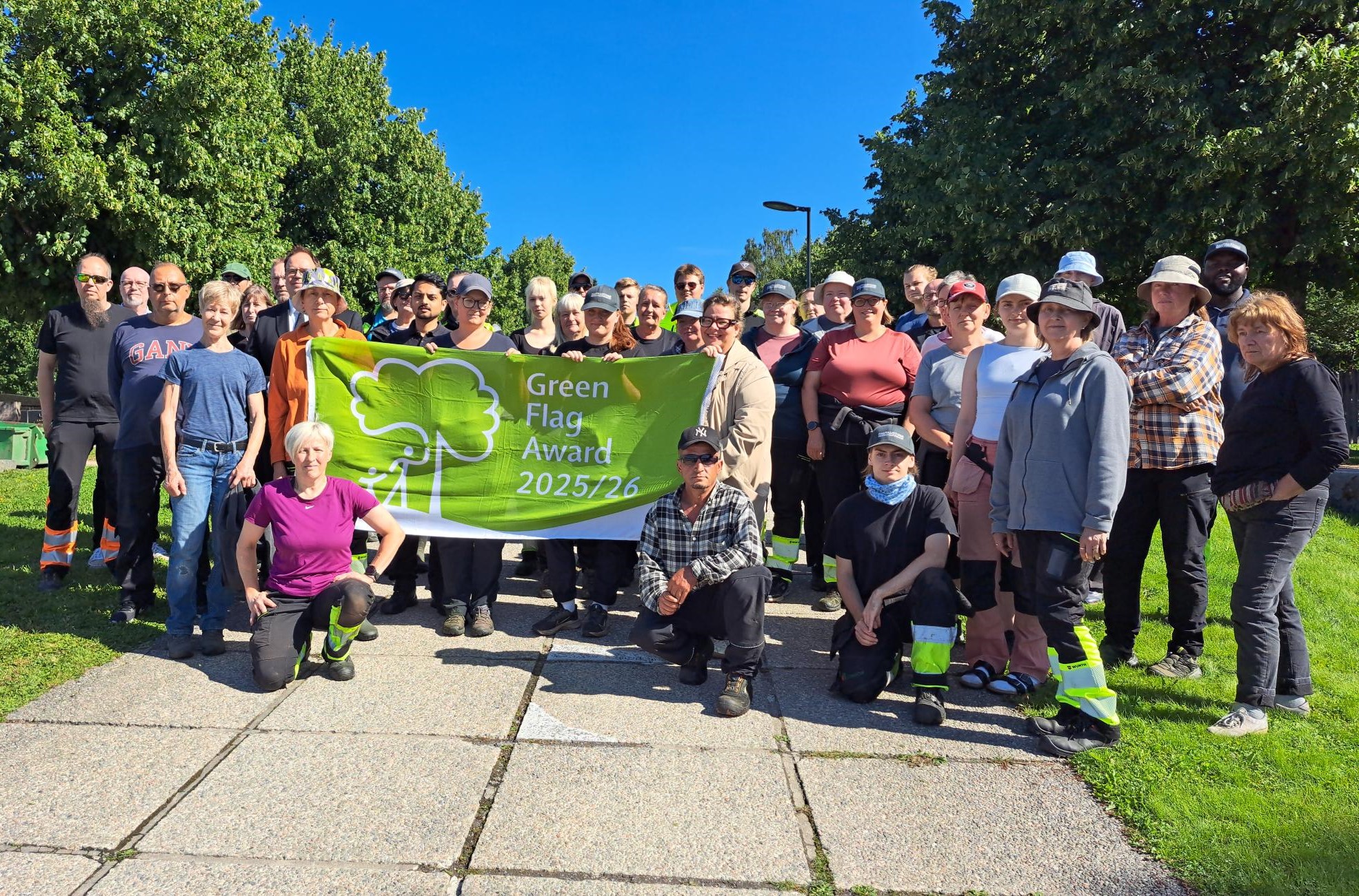 Ryhmä ihmisiä pitää esillä vihreää lippua tekstillä Green Flag Award 2025/26.