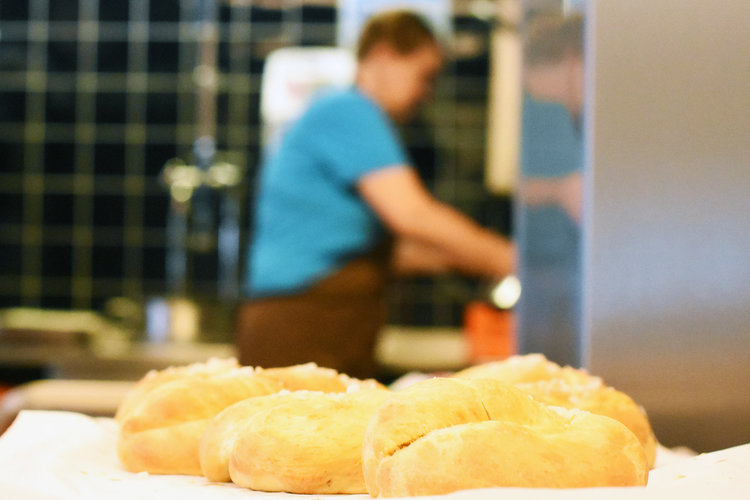 I förgrunden nygräddad bulle. I bakgrunden en kvinna som diskar.