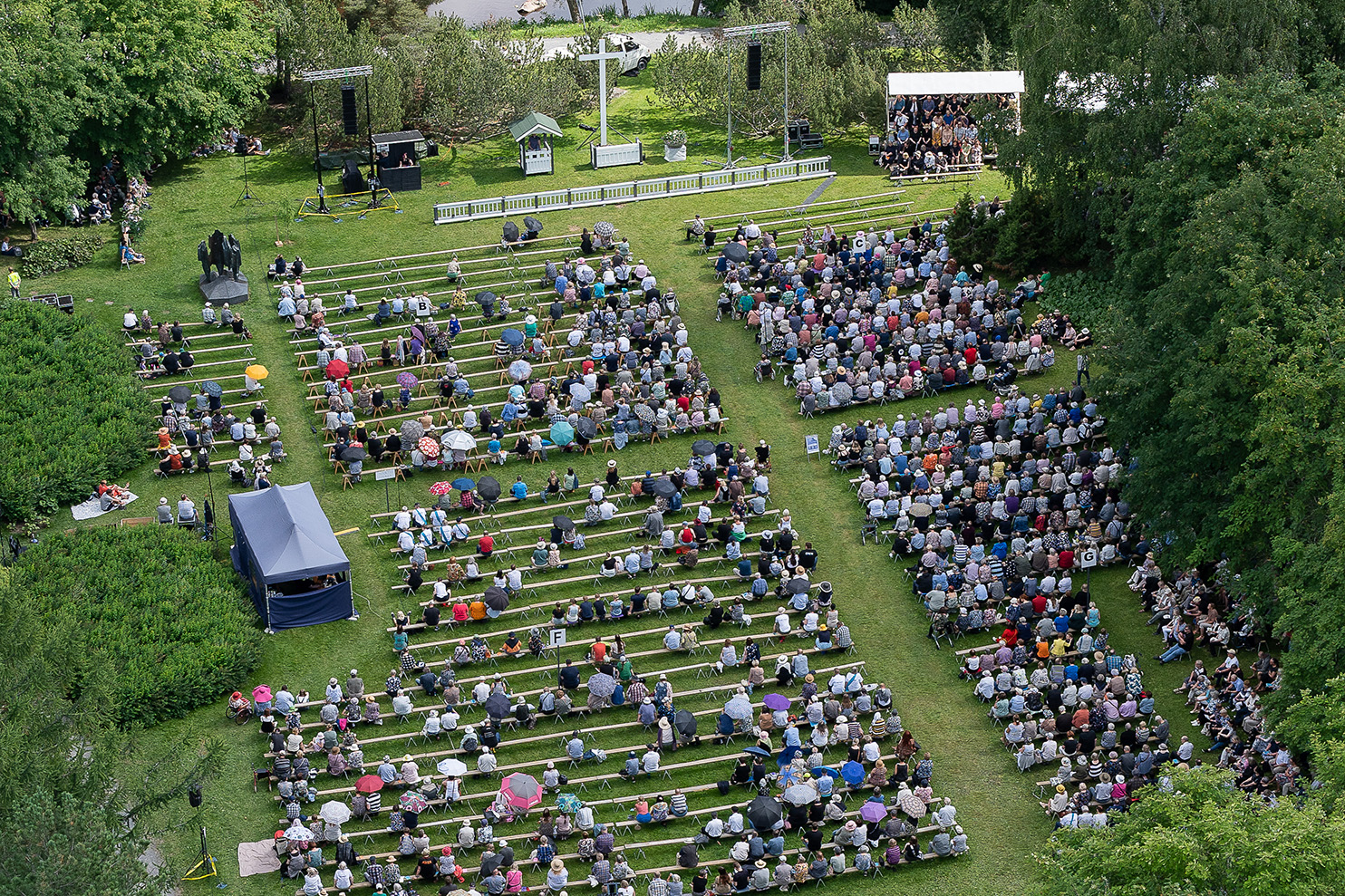 Paljon ihmisiä istuu penkeillä isolla kentällä.