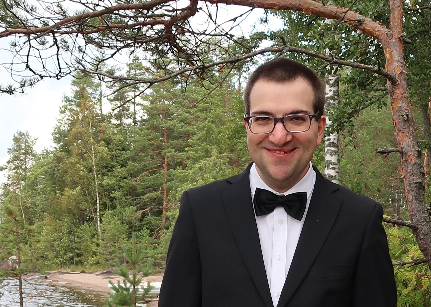 Mies seisoo ulkona, taustalla metsää.